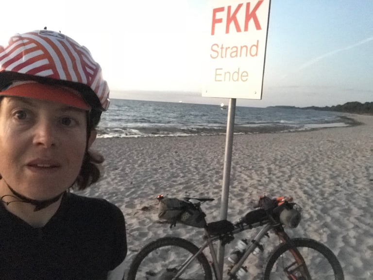 Emma Osenton selfie beside her loaded Kinesis and the FKK Strand Ende sign on Priwall beach at the Grenzsteintrophy finish.