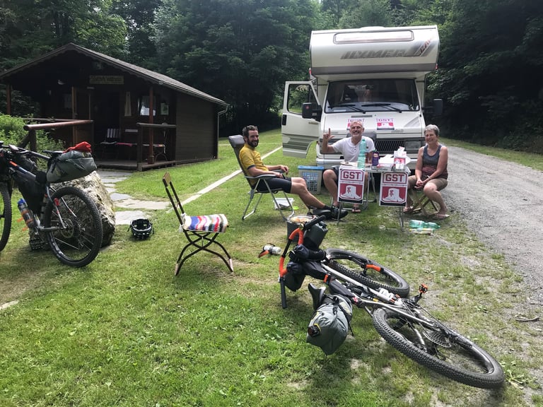 Volunteers at a motorhome aid point with GST signs on the Grenzsteintrophy route, bikes lying on the grass.
