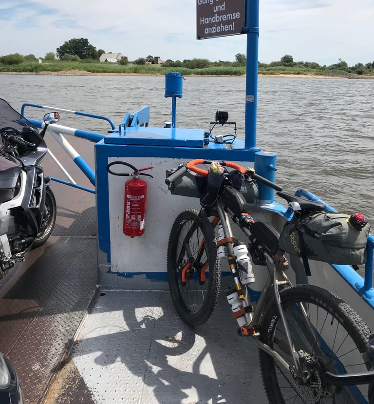 Loaded Kinesis mountain bike with Lauf fork and orange Jones loop bar leaning on a car ferry crossing the Elbe.