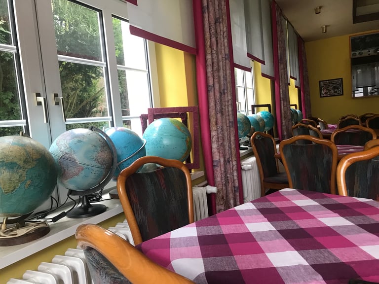 Hotel breakfast room with a row of globes on the windowsill and pink checked tablecloths.