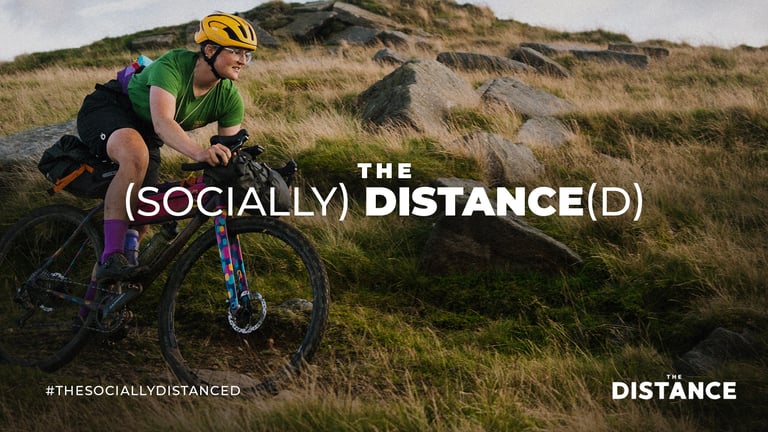 Rider in a yellow helmet with bikepacking bags climbs a rocky moorland slope on a second The (Socially) Distance(d) banner.