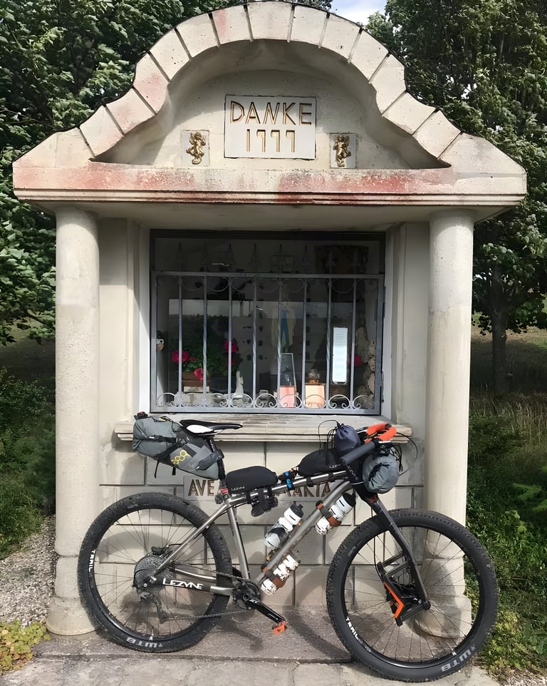 Kinesis Sync build with WTB tyres, Jones bars and bikepacking bags parked at a roadside shrine marked Danke.