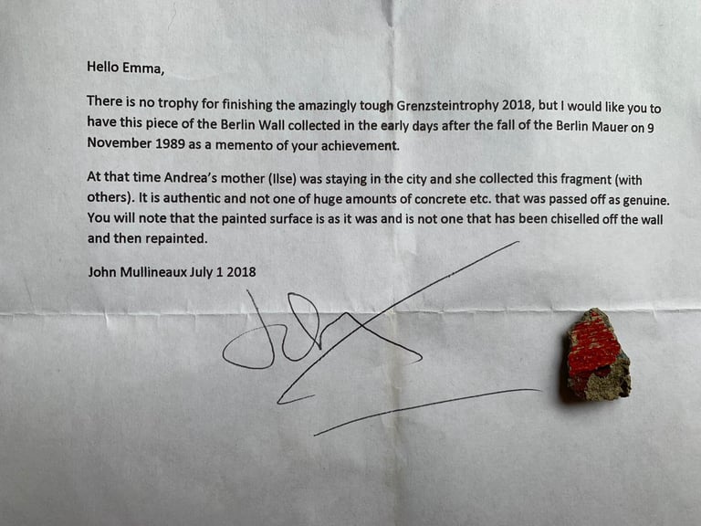 Letter marking Grenzsteintrophy 2018 finish, with a red-painted fragment of the Berlin Wall beside the signature.