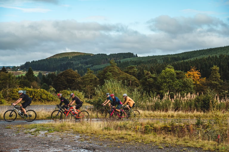 Five riders on a wet forest track below wooded hills, from the Frontier 300 coast-to-coast gravel event.