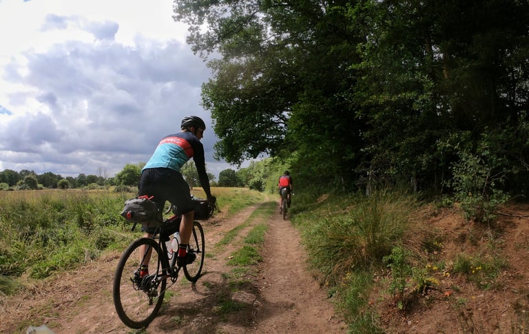 Two riders with bikepacking bags follow a rutted dirt track beside a field on Weaver's Way in Norfolk.