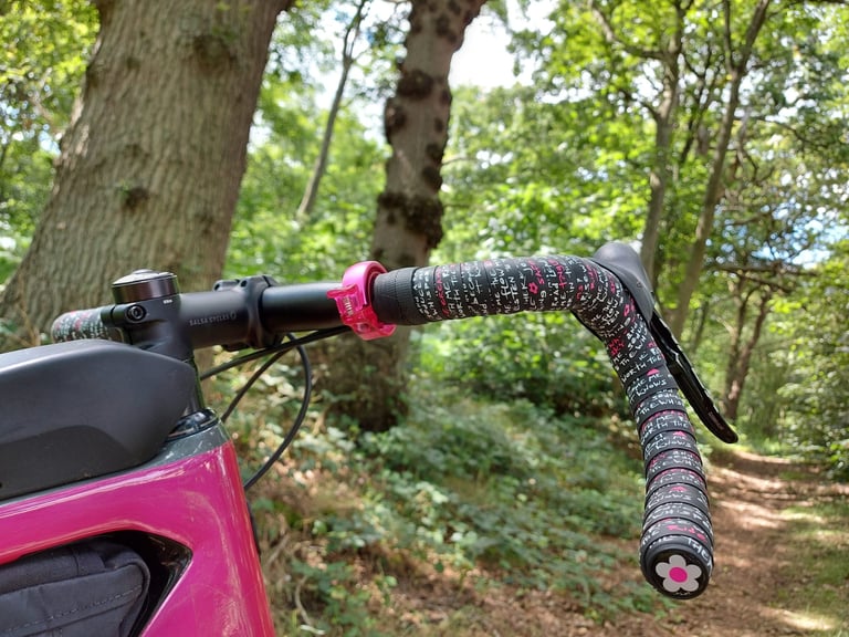 Kinesis Jo Burt signature bar tape on the drop bars of a pink Salsa Cutthroat, on a wooded trail.