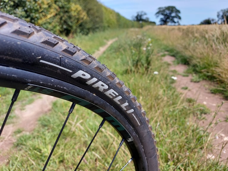 Pirelli lettering on a Cinturato Gravel M tyre mounted to a WTB i23 rim, with a grassy farm track behind.