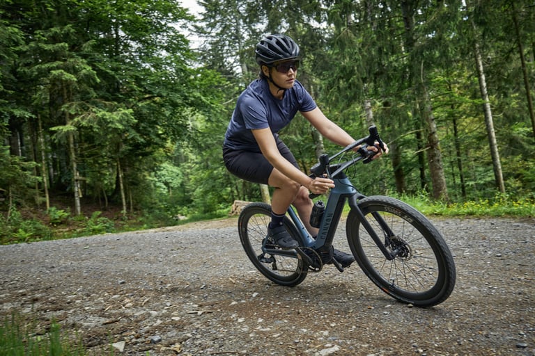 Rider on a Canyon Grail:ON eGravel bike rounds a gravel bend through pine forest.