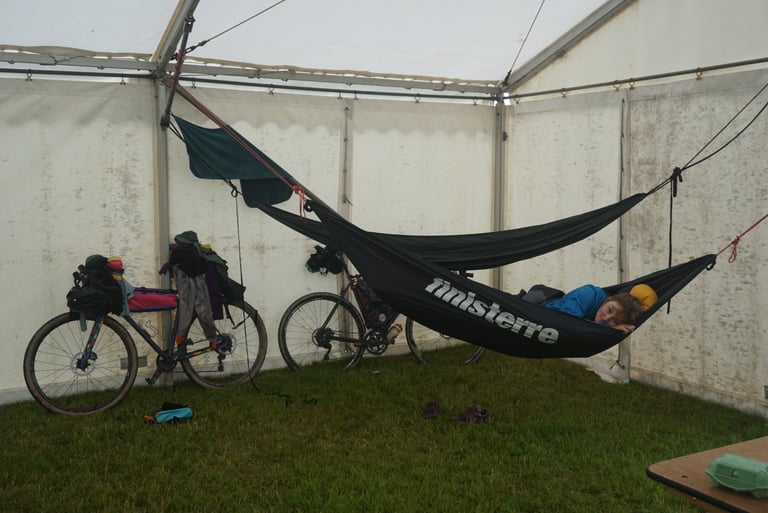 Rider lying in a Finisterre hammock strung from a marquee frame at the 2019 Gritfest, two bikepacking bikes on the grass.