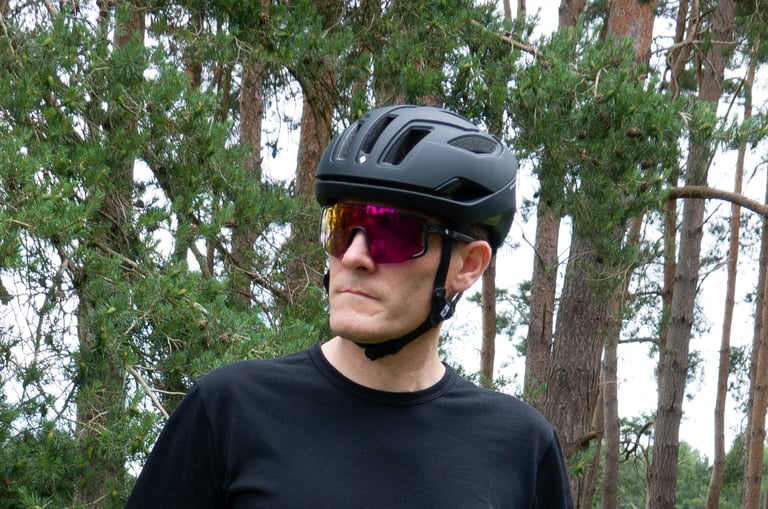 Rider wearing the Sweet Protection Falconer II helmet with pink-lensed sunglasses, among pine trees.