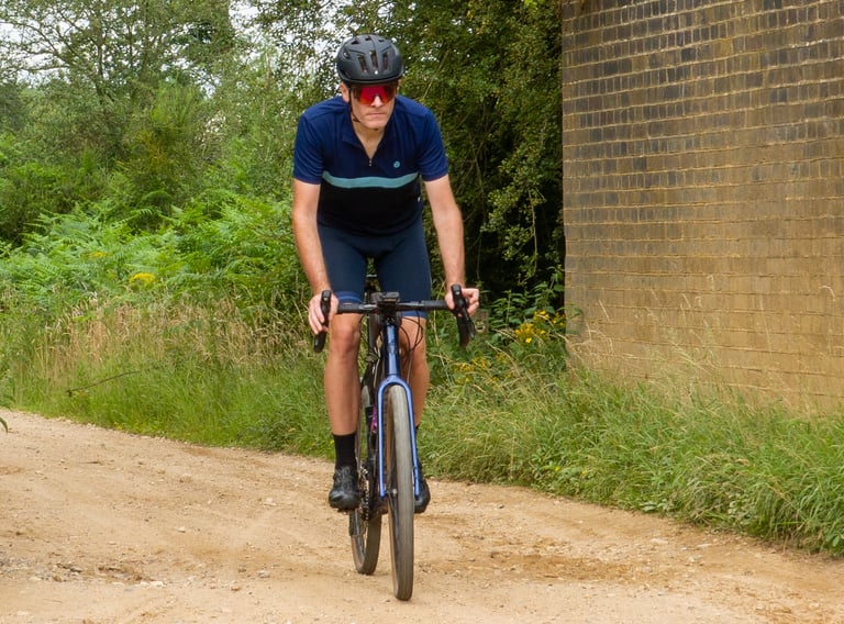 Rider in the colour block jersey and matching navy bib shorts on a gravel bike beside a brick wall.