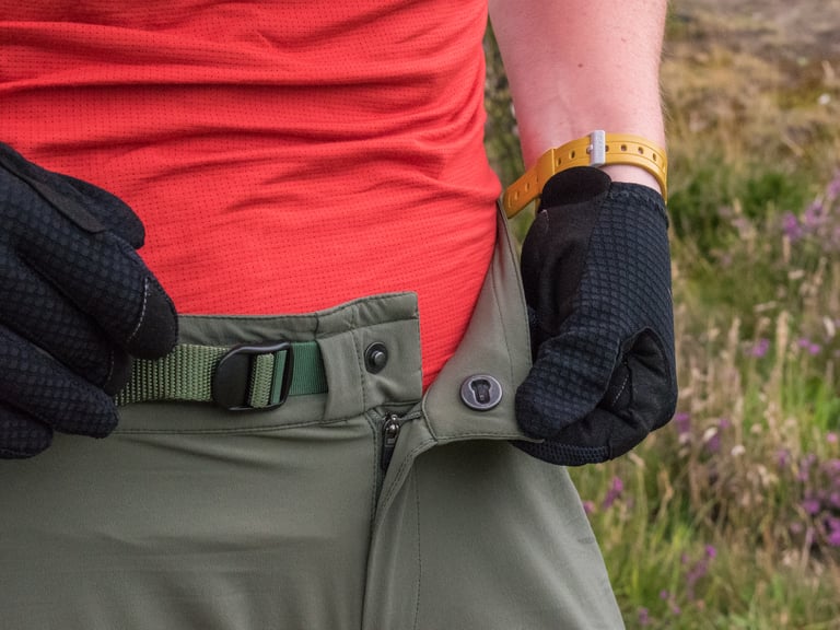 Close-up of the Velocio TRAIL Short waistband showing the slide-lock popper, YKK zip and webbing belt buckle.