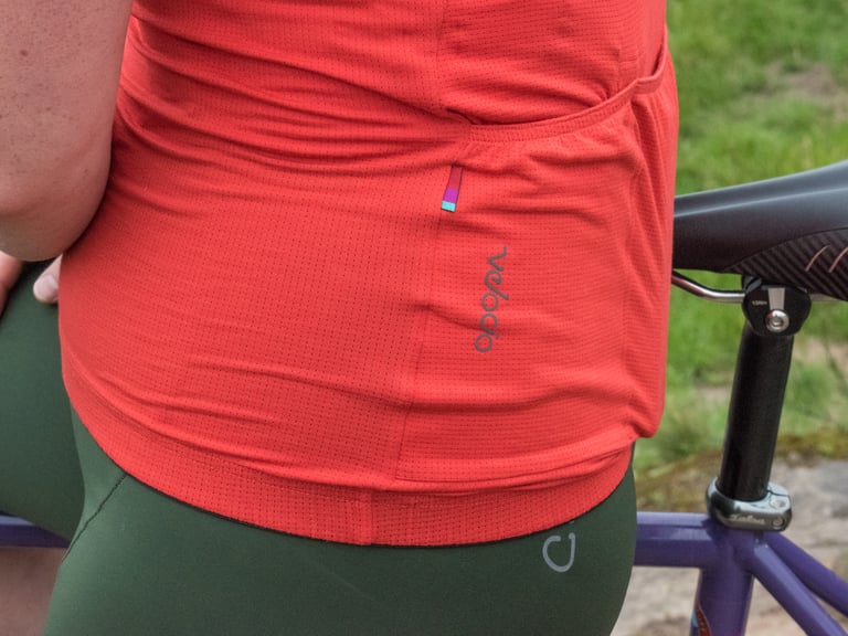 Close-up of the red Velocio Micromodal Jersey's rear pocket, perforated fabric and logo above the hem gripper.