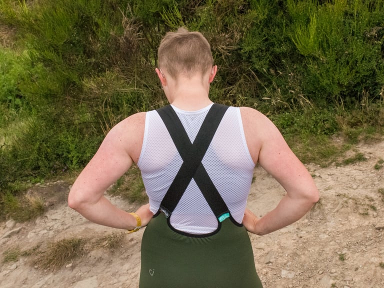 Rear view of Velocio LUXE bib shorts with crossed elastic straps and a high back panel, worn over a base layer.
