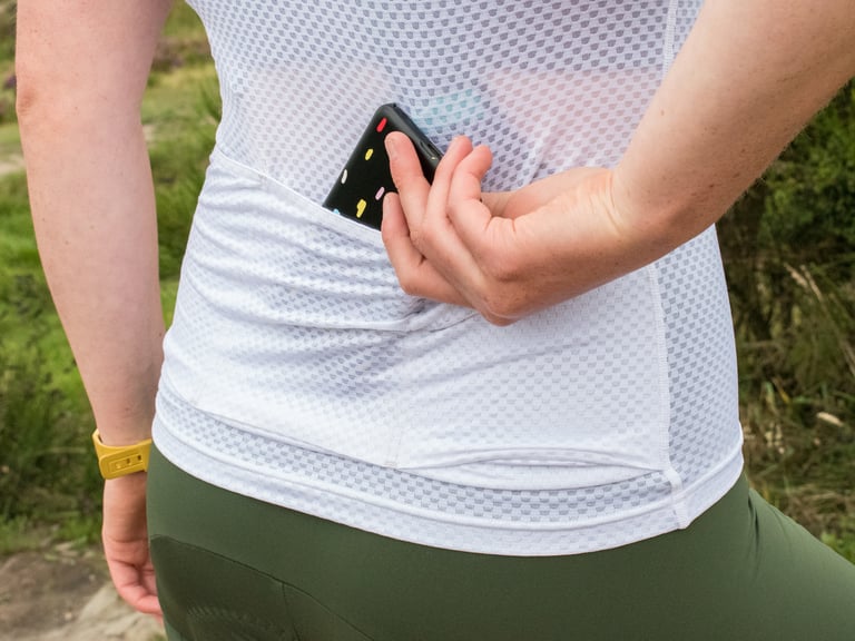 Hand pulling a phone from a rear pocket of the white mesh Velocio TRAIL Base Layer.