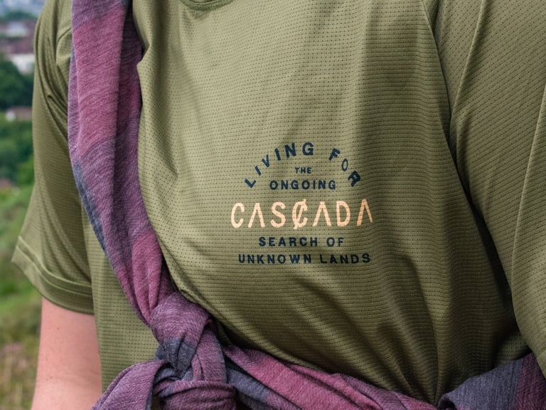 Chest of the green Cascada Trail Tee showing its perforated fabric and 'Living for the ongoing' logo print.