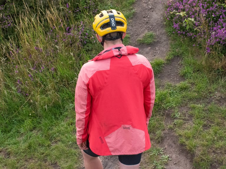 Rear view of the Infinium Hybrid Jacket worn on a trail, showing the lighter waterproof panel on the lower back.