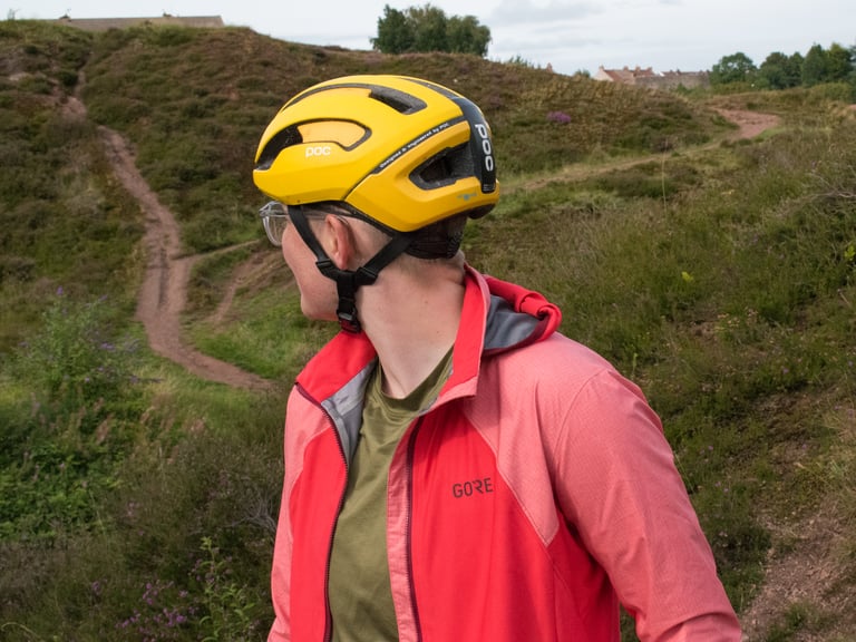 Katherine Moore in a yellow POC helmet and the pink Infinium Hybrid Jacket looks back along a heathland track.