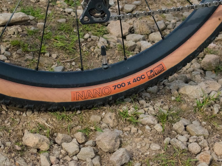 WTB Nano 700 x 40C tan-wall tubeless tyre on the Mercredi's rear wheel, resting on stony ground.