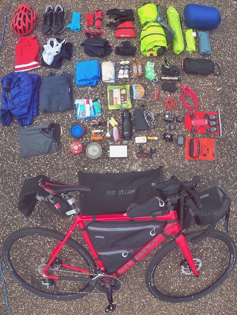 Matt's red Thompson R9300 gravel bike with Alpkit frame bag and his bikepacking kit laid out in a grid above it.
