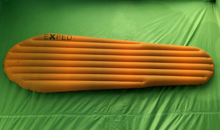 Inflated Exped SynMat HL M in orange with a honeycomb pattern, laid flat on a green tent groundsheet.