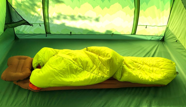 Yellow sleeping bag laid over the Exped SynMat HL M and inflatable pillow inside a green tent.