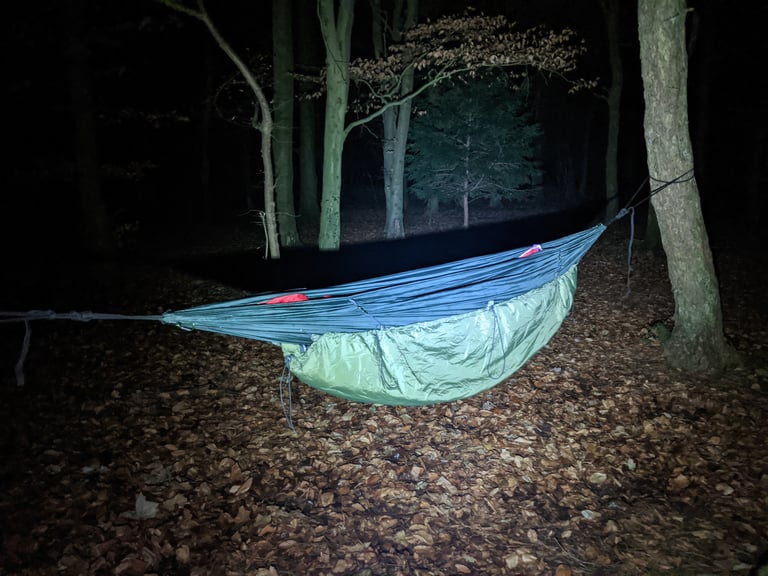 DD Hammock Underblanket slung under a hammock in woods at night, lit by a torch.