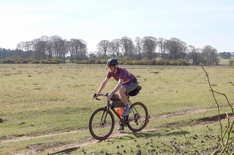 Side view of a rider in the Stolen Goat Merino Gravel Jersey on a gravel bike with a saddlebag across open heathland.