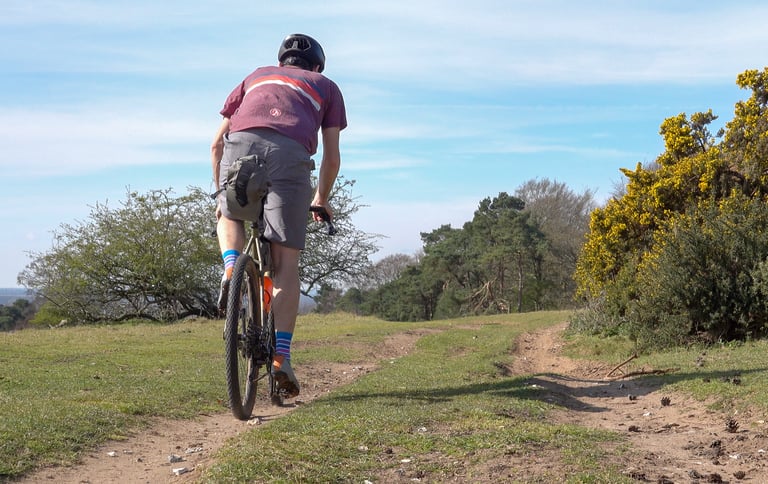 Rear view of the Stolen Goat Merino Gravel Jersey on a rider climbing a dirt track, with a saddlebag on the bike.