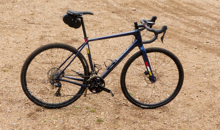 Side view of the blue Salsa Warbird GRX 600 on a stony dirt track, fitted with a small saddle bag.