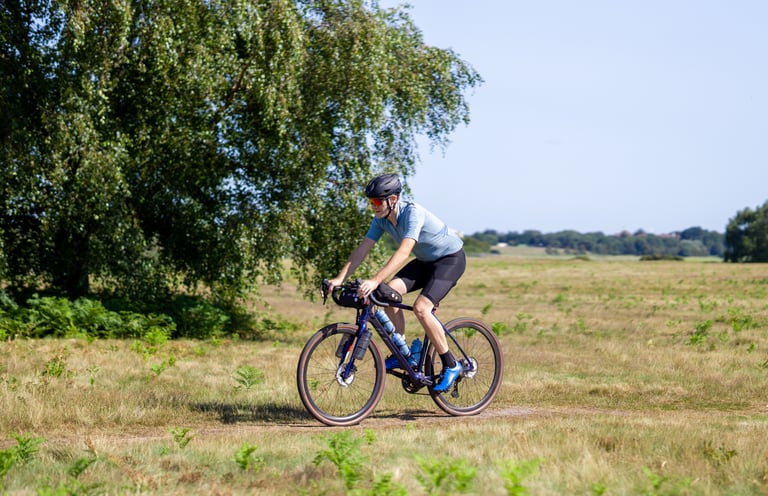 Rider in a light blue jersey on the Salsa Warbird follows a grassy track across open heathland.