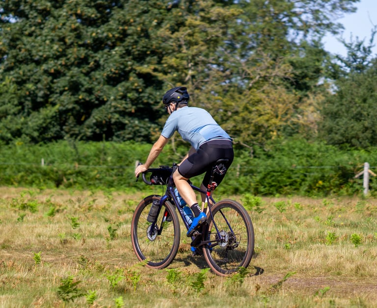Rider on the Salsa Warbird seen from behind, pedalling a grass trail past ferns on a sunny day.