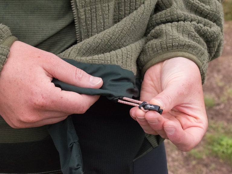 Hands hold the valve core tool built into a drawcord toggle on the hem of the Rapha Explore Technical Hoodie.