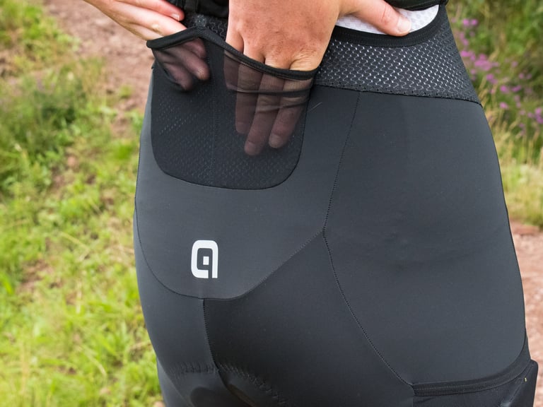 Rear of the Alé Stones cargo bib shorts with a hand reaching into one of the two lower-back mesh pockets.