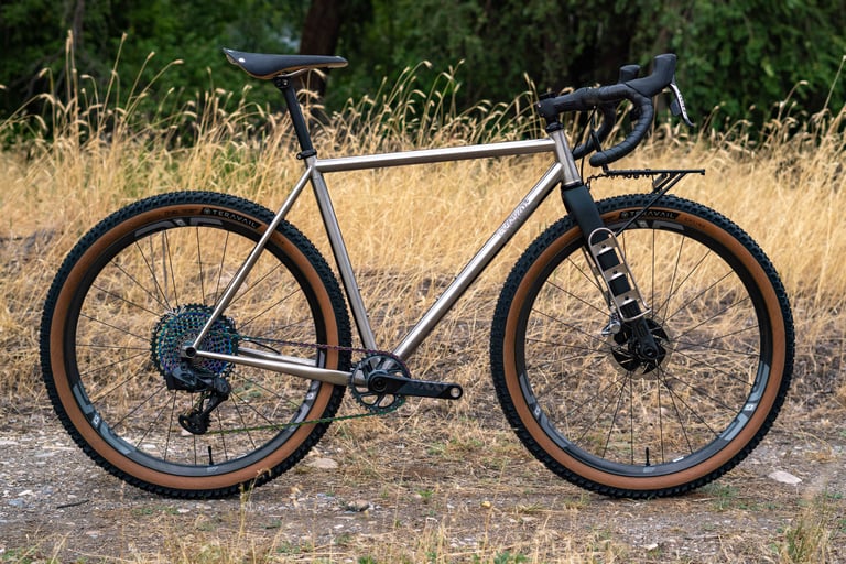 Unpainted gravel bike with an ENVE Adventure Fork carrying a fork-mounted cage, on tan-wall Teravail tyres.