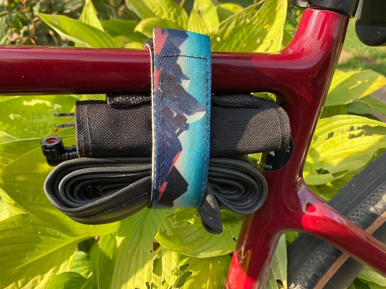 Granite ROCKBAND+ strap holds a tool roll and spare inner tube against the top tube of a dark red gravel bike.