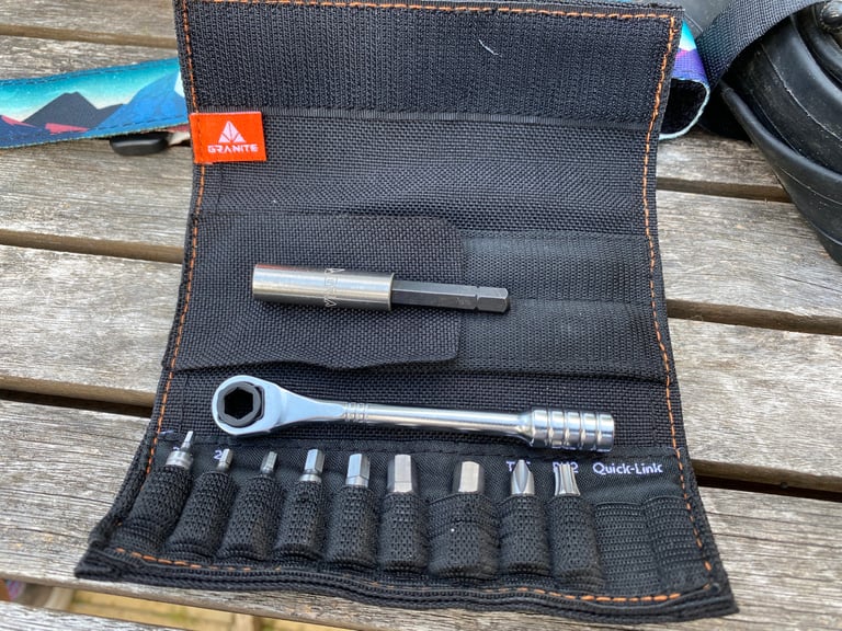 Open Granite ROCKnROLL tool roll with mini ratchet, extension rod and nine bits on a wooden table.