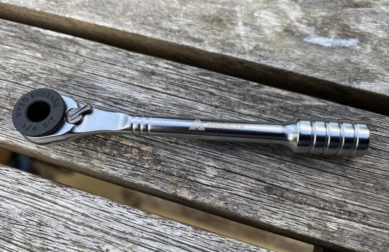 Close-up of the Granite ROCKnROLL mini ratchet with reverse gear and 1/4 bit socket on weathered wood.