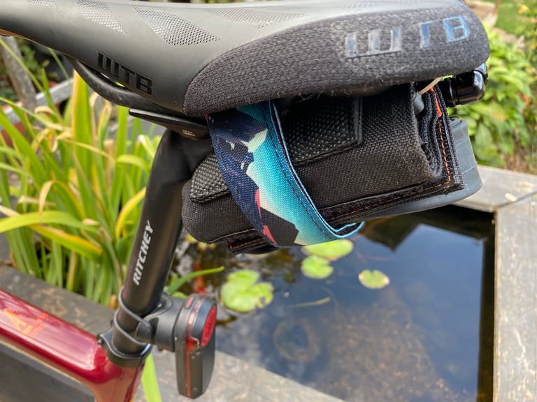 Granite ROCKBAND+ holding a tool roll under a WTB saddle, with a rear light on the seatpost and a pond behind.