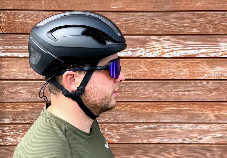 Side profile of a rider in a black helmet wearing Rapha Explore Glasses, the neck strap hanging from the arm.