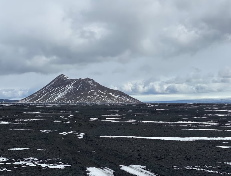 Askja volcano rising above a black lava plain streaked with snow on the Iceland Divide.