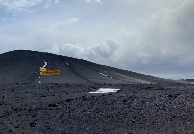 Yellow F98 signpost pointing to Nyidalur, 95 km, on a black volcanic plain on the Iceland Divide.