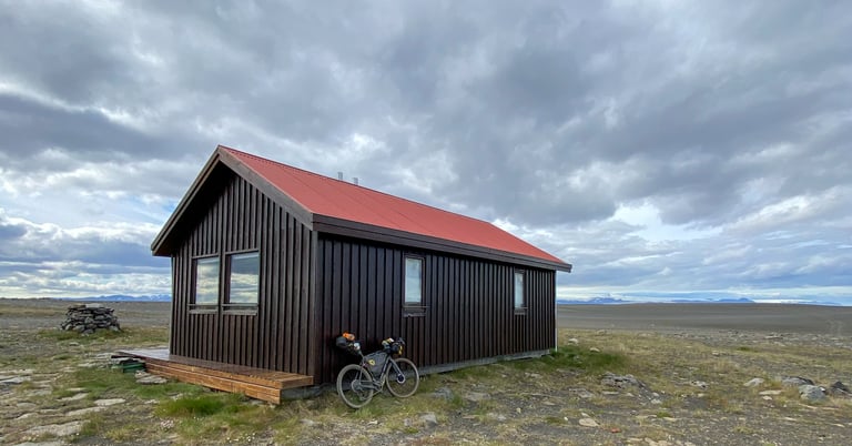 Loaded Bombtrack bikepacking bike leans on the red-roofed Nyidalur mountain hut on the open Iceland Divide plateau.