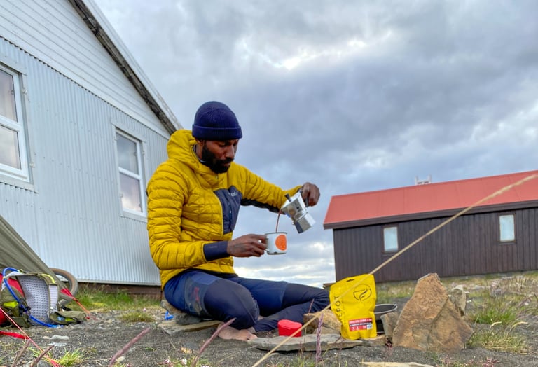 Natt Williams pours Moka pot coffee outside a mountain hut, a Firepot meal pouch beside him on the Iceland Divide.
