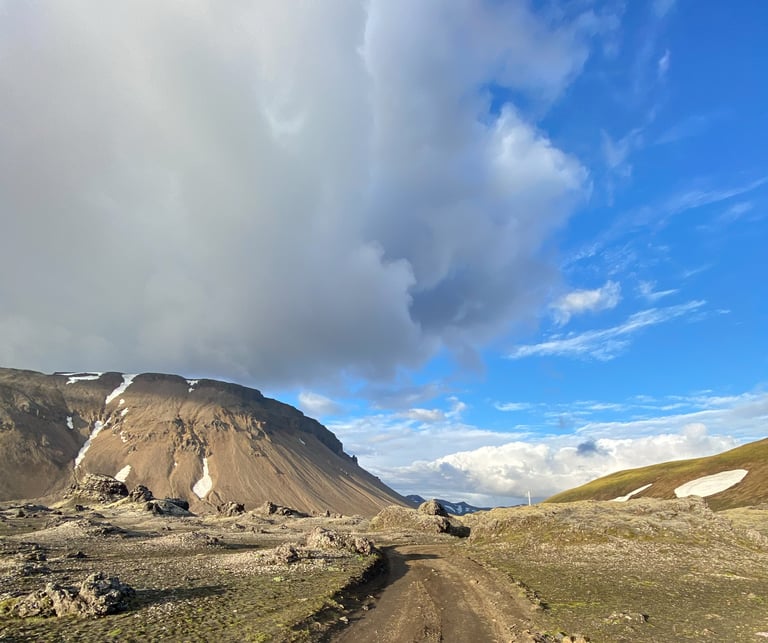 Dirt track winds through lava fields below a brown mountain towards the Gate to Valhalla climb on the Iceland Divide.