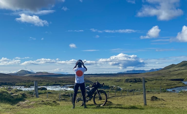 Natt Williams adjusts his helmet beside a loaded gravel bike, a river and green hills behind, the Iceland Divide done.