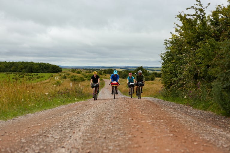 Four bikepackers ride a wide gravel road across Salisbury Plain on the King Alfred's Way.