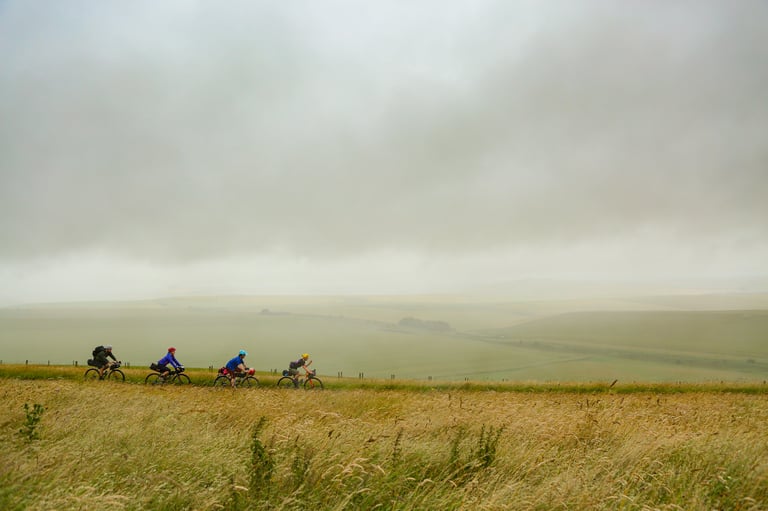 Four bikepackers ride the South Downs Way on a misty, overcast morning after a wet night camping.