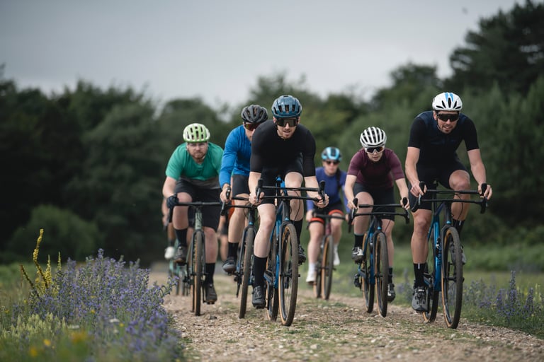 Bunch of riders on gravel bikes along a wildflower-lined gravel track, the fast, flat racing the King's Cup promises.
