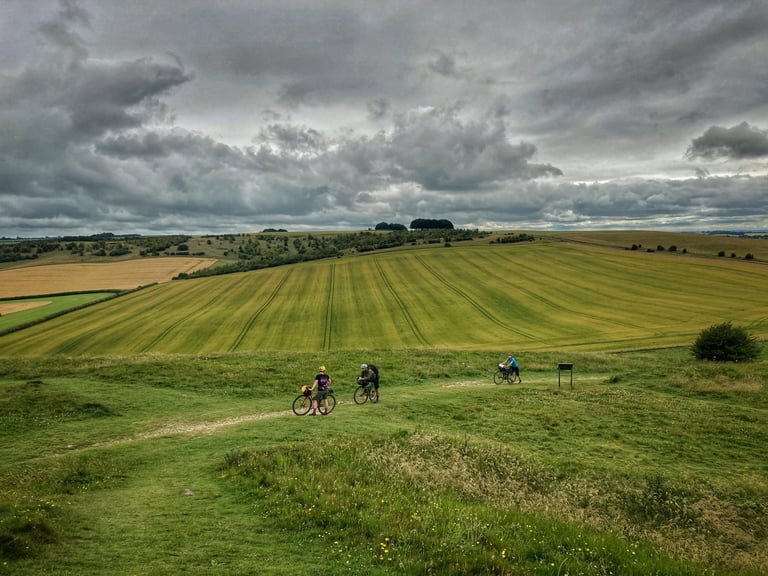 Three riders cross the grassy ramparts of Barbury Castle on the King Alfred's Way as it climbs onto the Ridgeway.